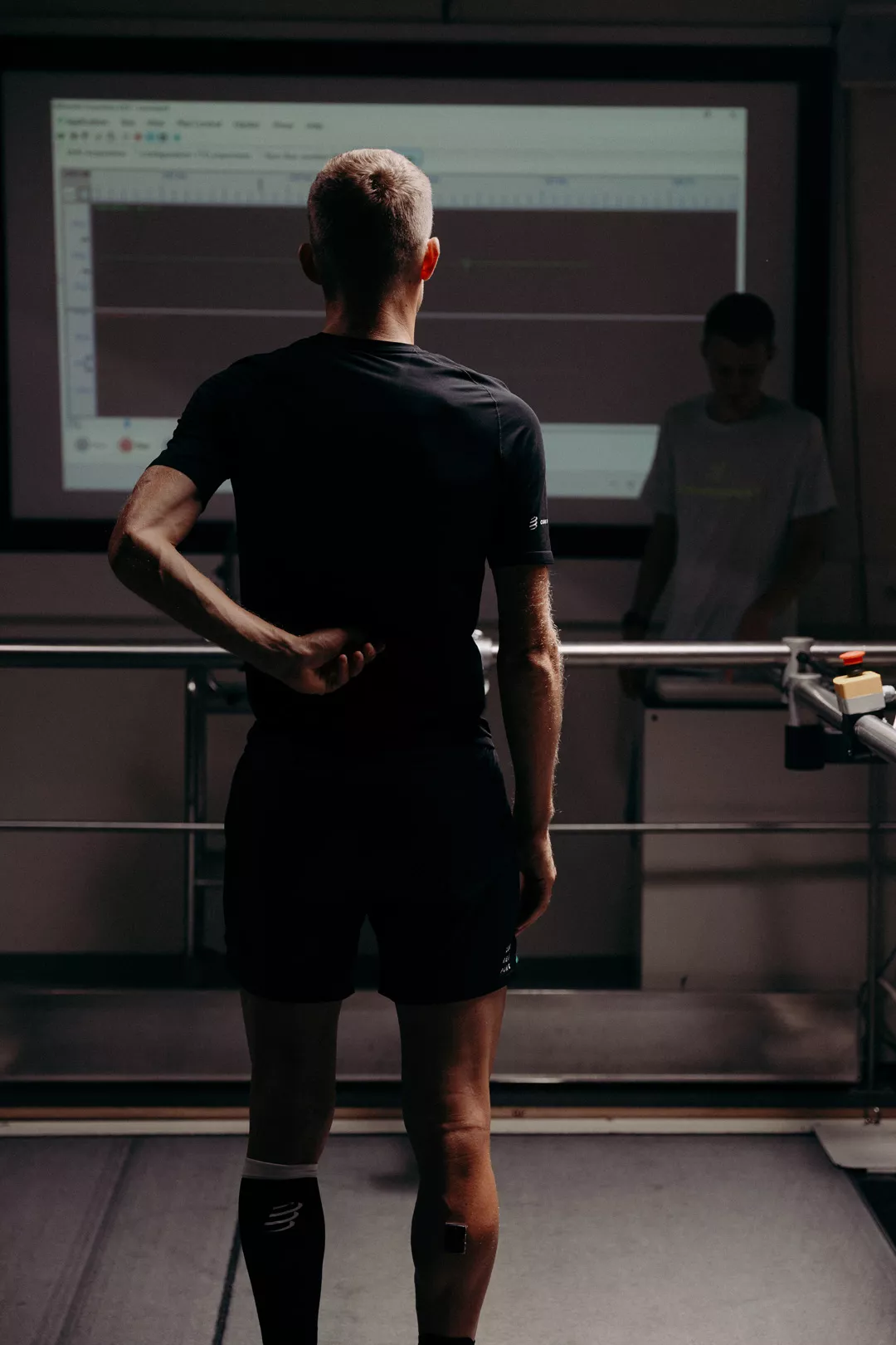 Athlete on a treadmill in the Compressport Lab, facing a screen of test data