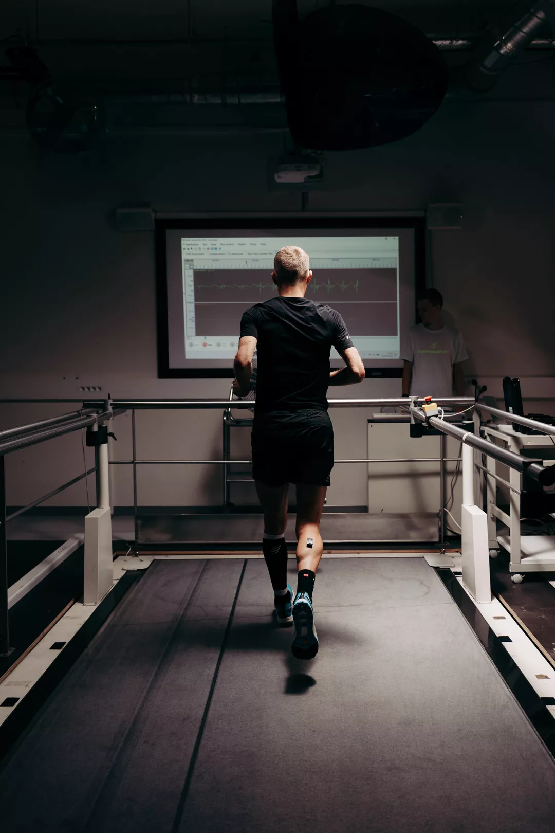 Athlète de dos sur tapis de course devant l'écran d'analyse du Lab Compressport